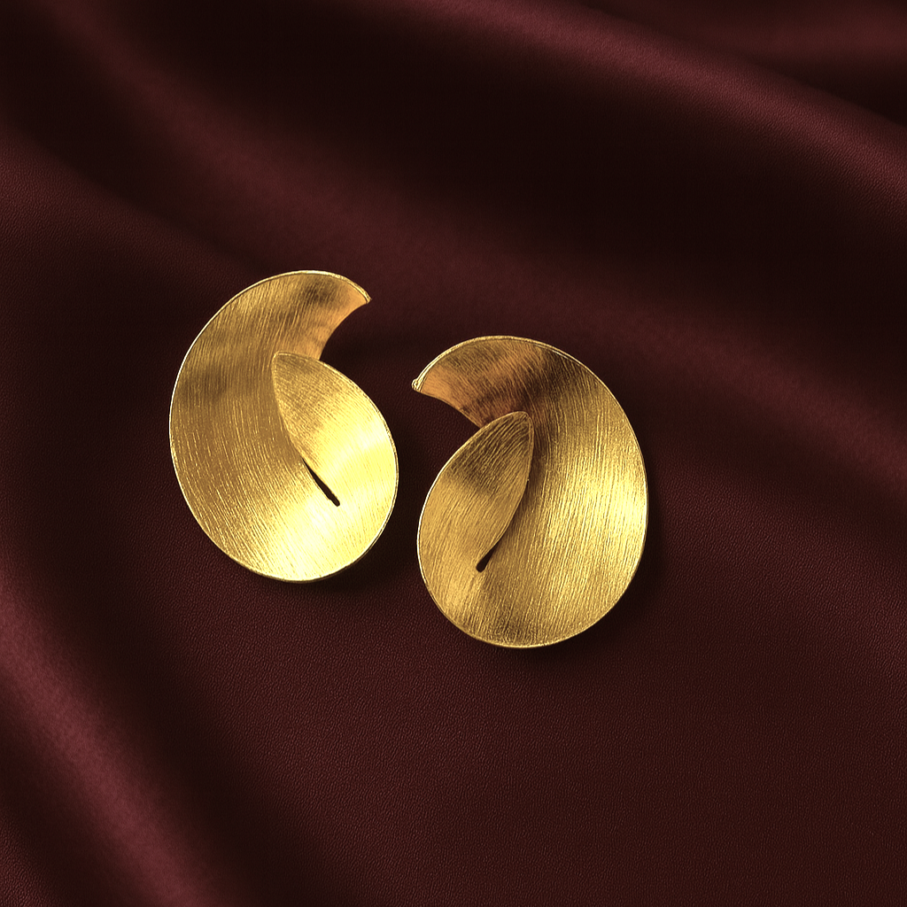Masaira Sculptural Swirl Brushed Gold-Plated Statement Stud Earrings Masaira gold-plated sculptural swirl earrings with brushed texture on deep maroon satin