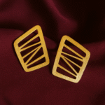 Modern cutout gold earrings with asymmetric windowpane design on maroon silk backdrop