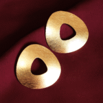 Minimalist gold-plated geometric earrings with hollow organic triangle shape on maroon satin fabric