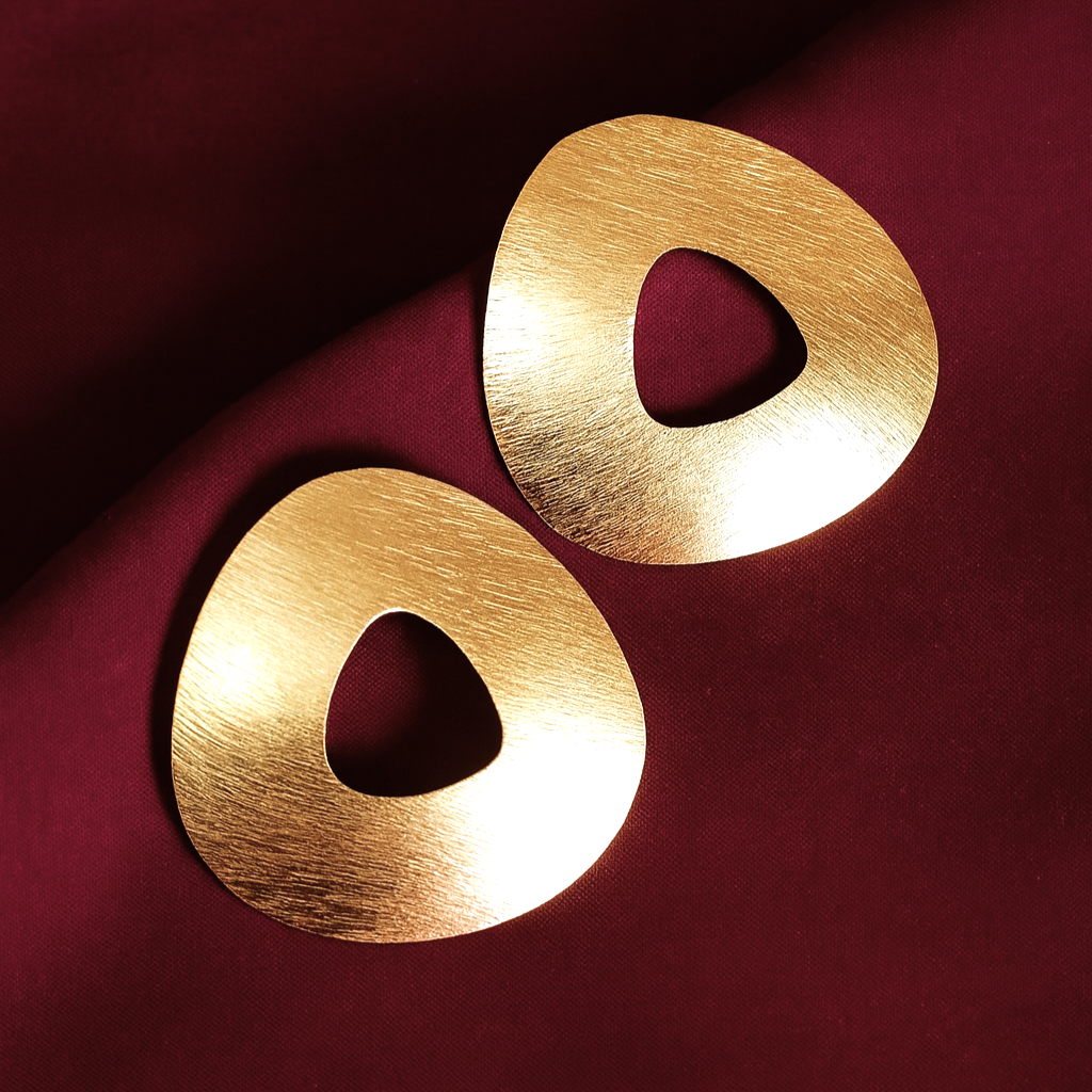 Minimalist gold-plated geometric earrings with hollow organic triangle shape on maroon satin fabric
