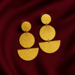 Textured matte gold earrings with stacked circle and semi-circle elements on maroon silk fabric