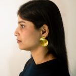 Left profile: model wearing Masaira Sculptural Swirl brushed gold-plated statement stud earring