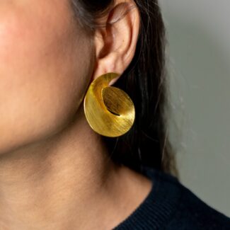 On-ear close-up: model wearing Masaira Sculptural Swirl brushed gold-plated statement stud earring