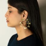 Left profile: model wearing Masaira Laurel gold-plated hoop earring with leaf motifs