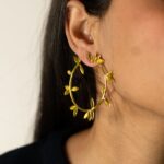 On-ear view showing Masaira Laurel gold-plated hoop with laurel leaves — front angle