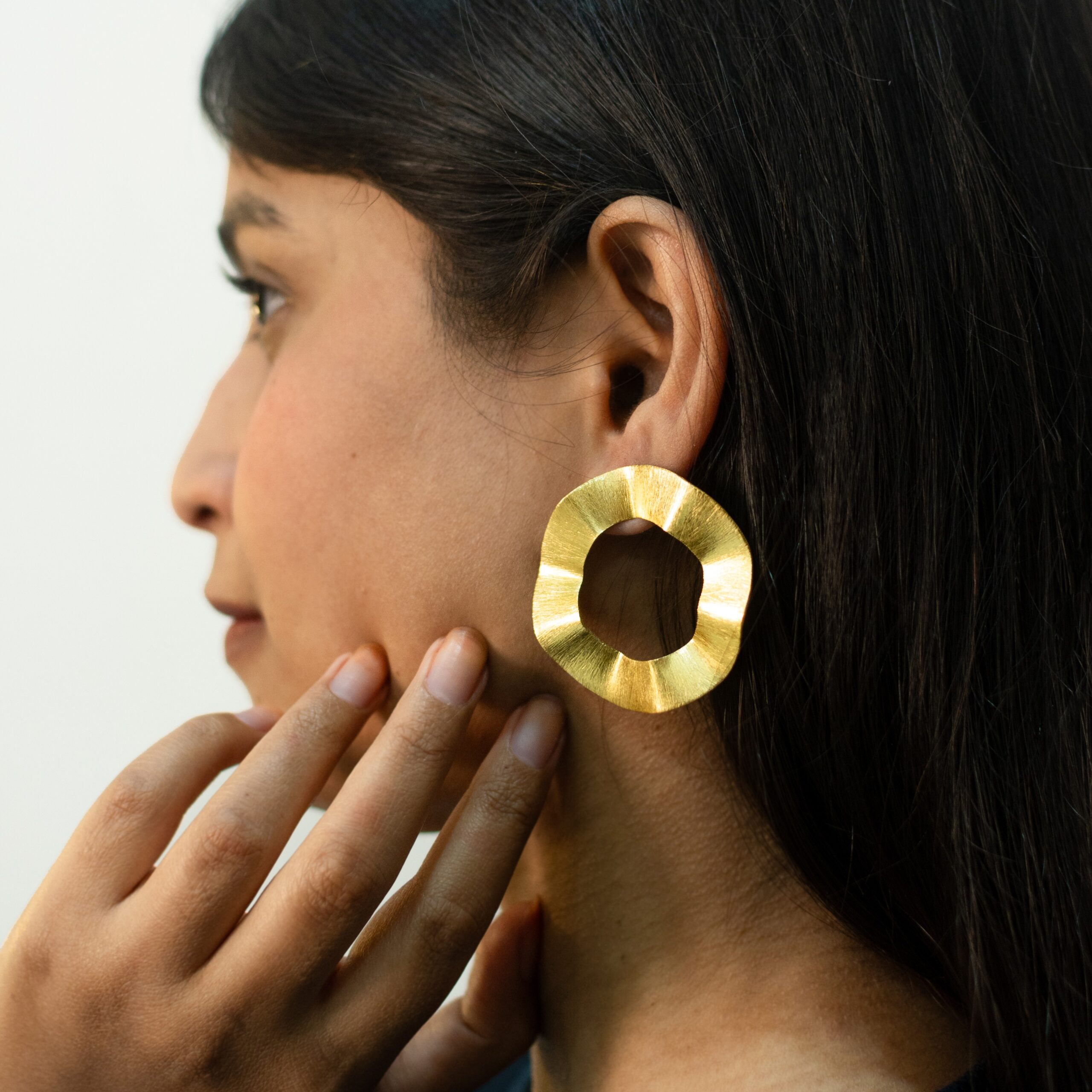 Front-leaning close-up: Masaira Ripple Halo brushed gold-plated wavy open-circle stud