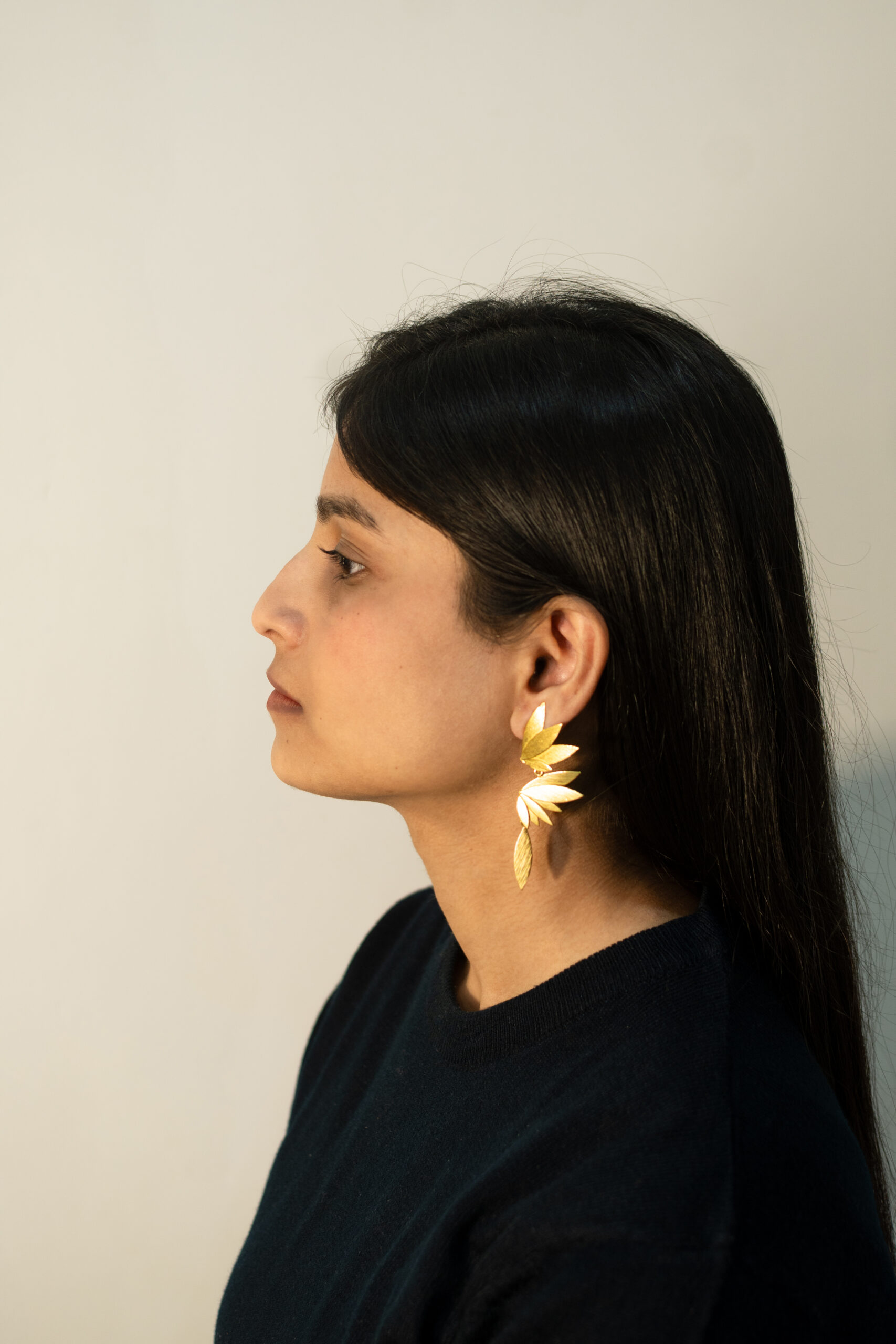 Side profile view of Phoenix Earrings in gold plated design, styled with sleek hair and dark outfit.