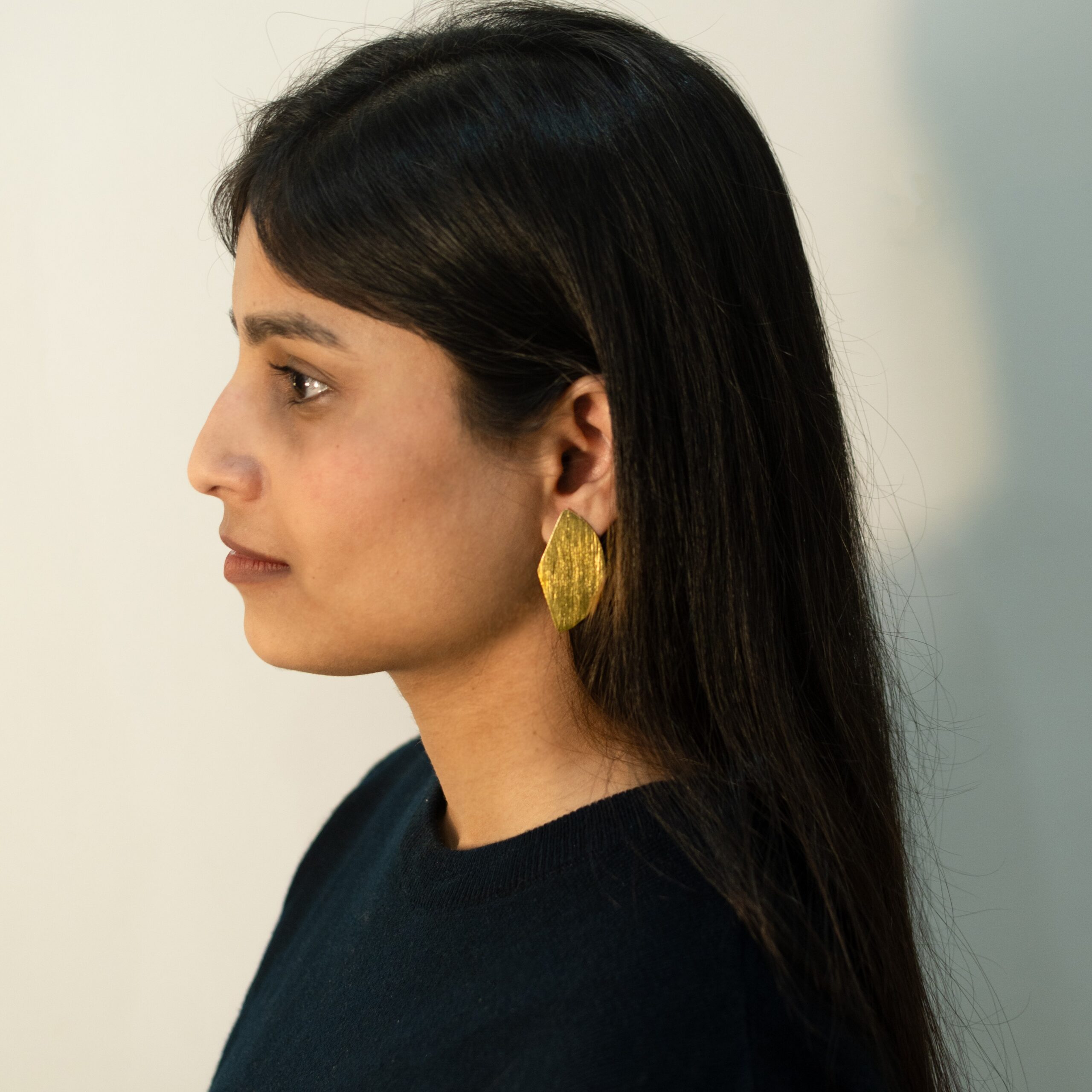 Left profile: model wearing Masaira Split Circle gold-plated asymmetrical stud (tapered half) with brushed texture