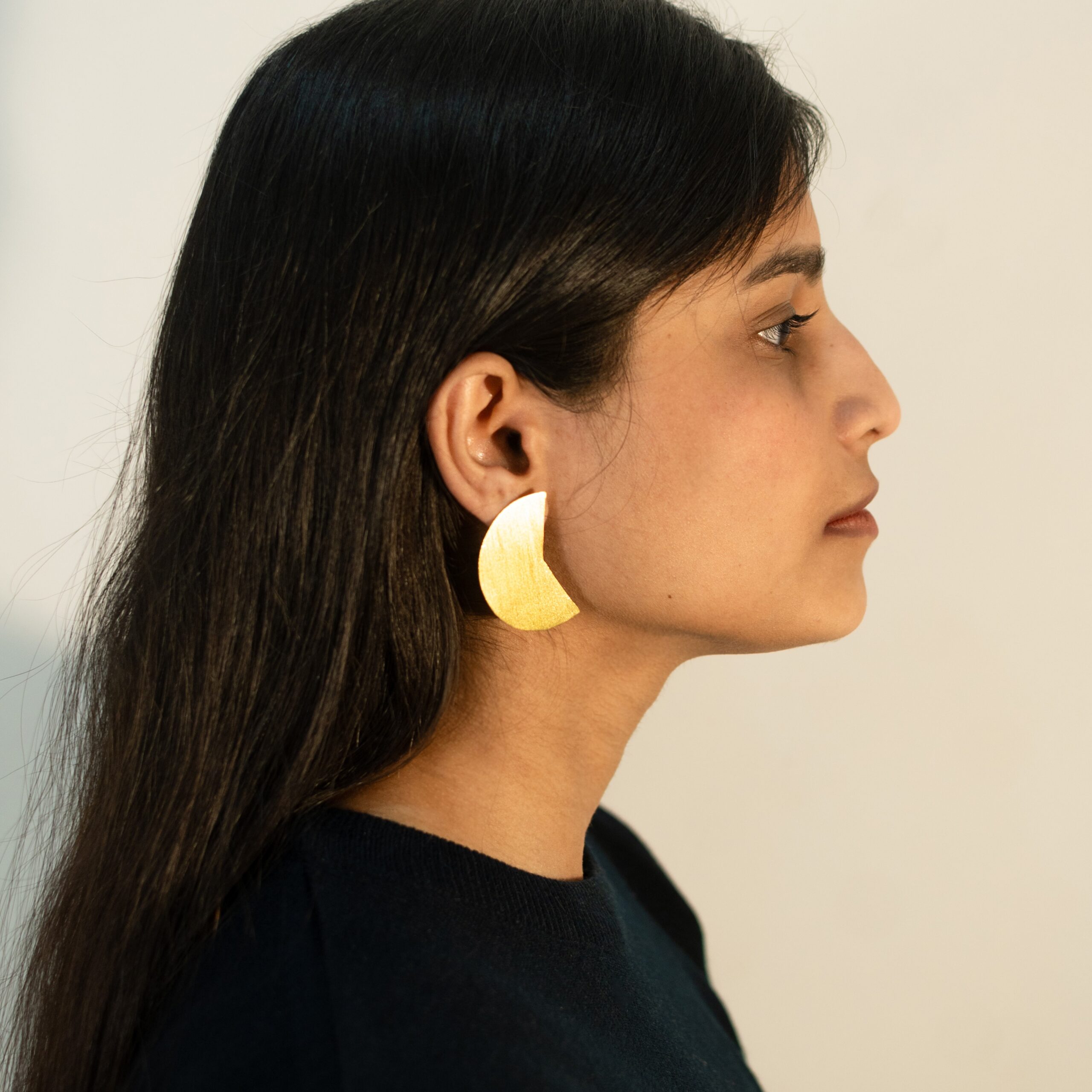 Right profile: model wearing Masaira Split Circle gold-plated asymmetrical stud (curved wedge half) in brushed finish