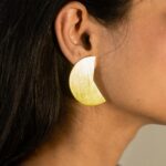 Right ear close-up: Masaira Split Circle gold-plated wedge stud — asymmetrical half of one split circle, brushed finish