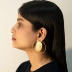 Left-facing profile: model wearing Masaira Orbit gold-plated open-hoop earring with brushed oval disc