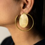 Close-up left ear wearing Masaira Orbit gold-plated open-hoop earring with brushed oval disc