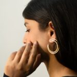Close detail with hand: Masaira Double Arc gold-plated twin-band open hoop earring