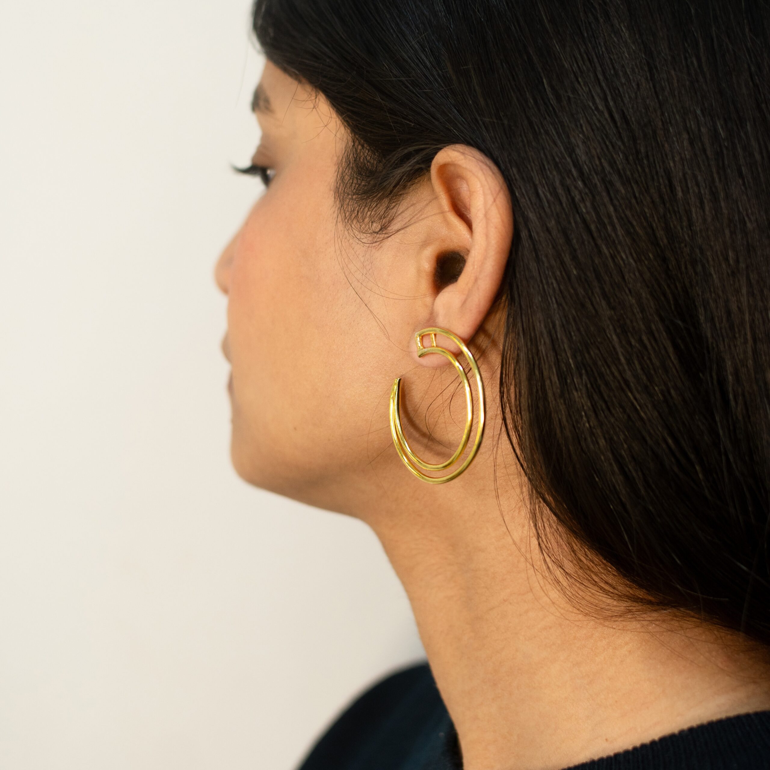 Three-quarter close-up: Masaira Double Arc gold-plated open hoop showing twin bands and open end