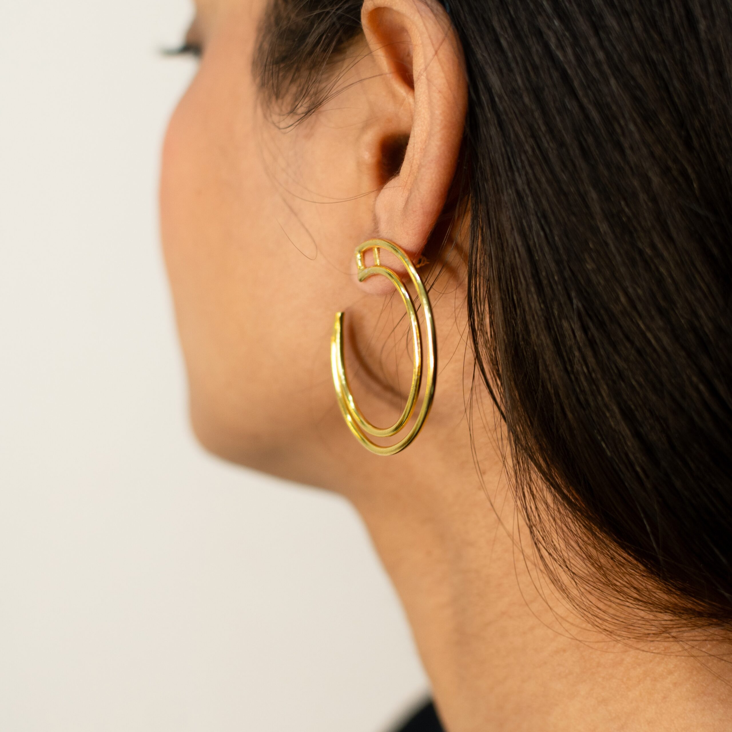 Rear three-quarter: model wearing Masaira Double Arc helix gold-plated double-band open hoop