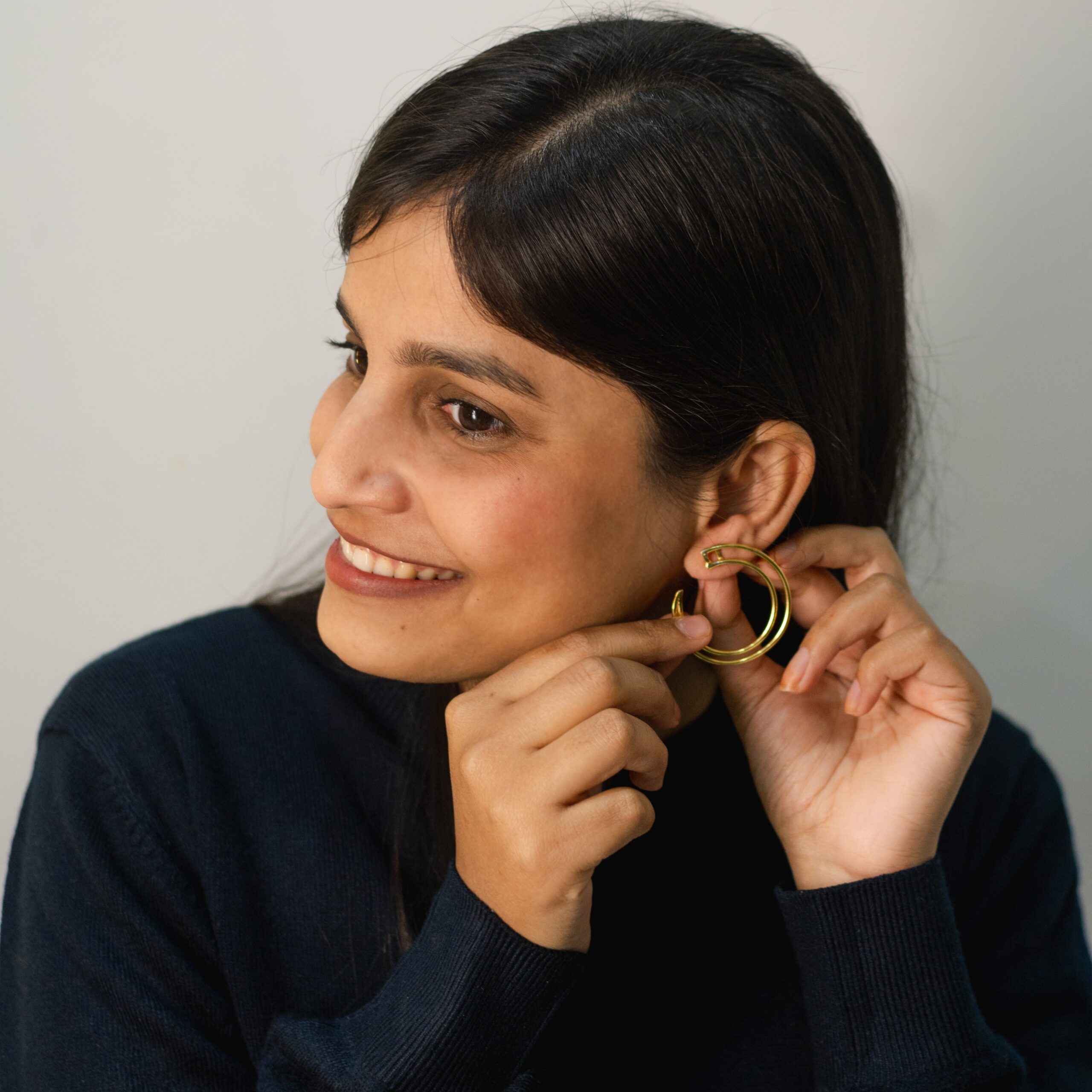 Model putting on Masaira Double Arc gold-plated double-band open-hoop earring, smiling three-quarter view