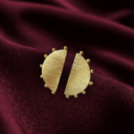 Masaira Eclipse gold-plated half-moon stud earrings with brushed texture and beaded edge on deep maroon satin
