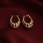 Minimalist triangular brushed gold-plated earrings on maroon satin fabric
