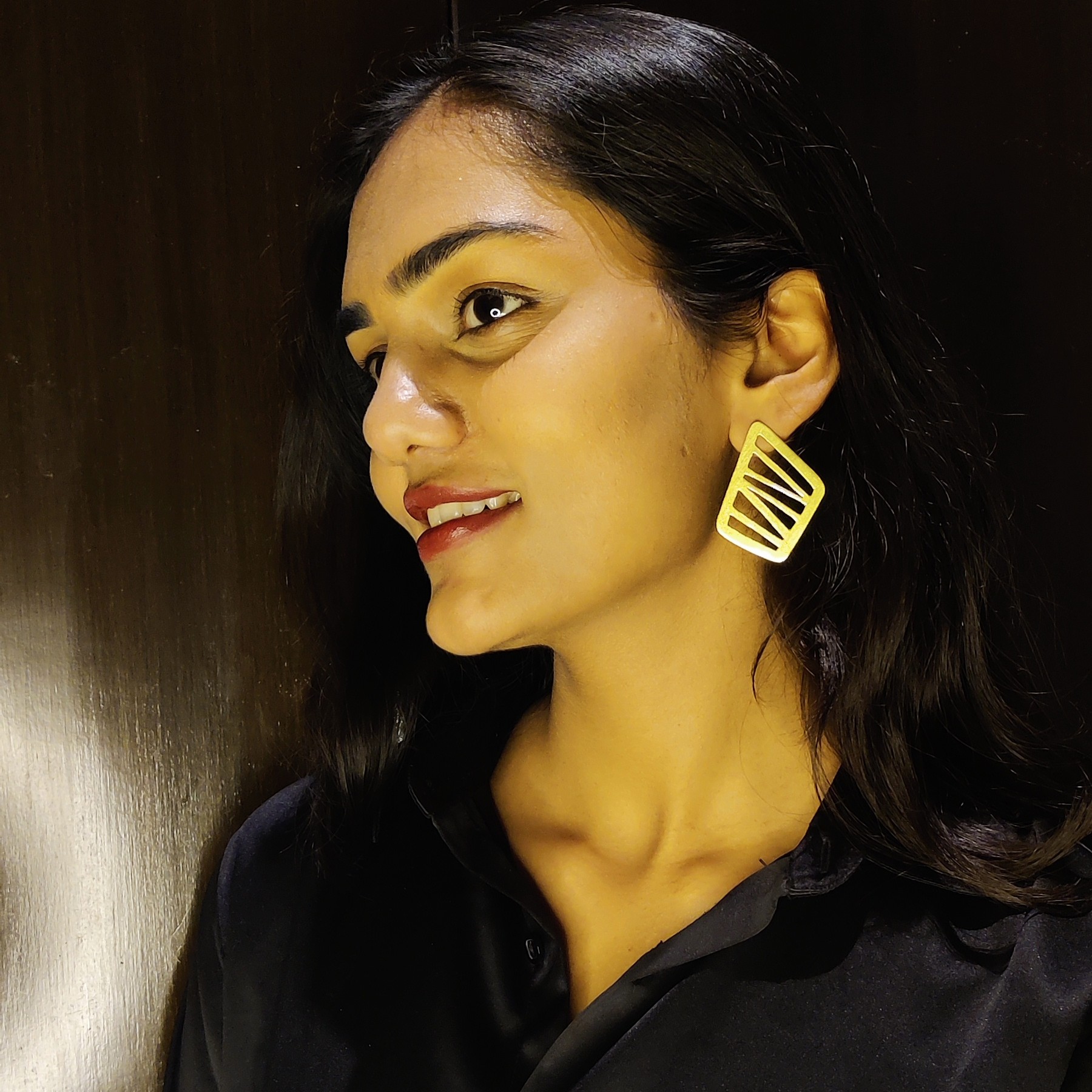Modern Geometric Cut-Out Gold Statement Earrings – Lightweight & Bold Design Indian woman wearing modern geometric gold earrings with bold cut-out design, side profile view, dark background.