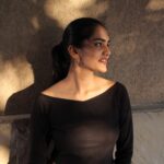 Model in black top wearing Masaira Luna Drop huggie earrings, warm sunlight creating soft highlights on polished gold.