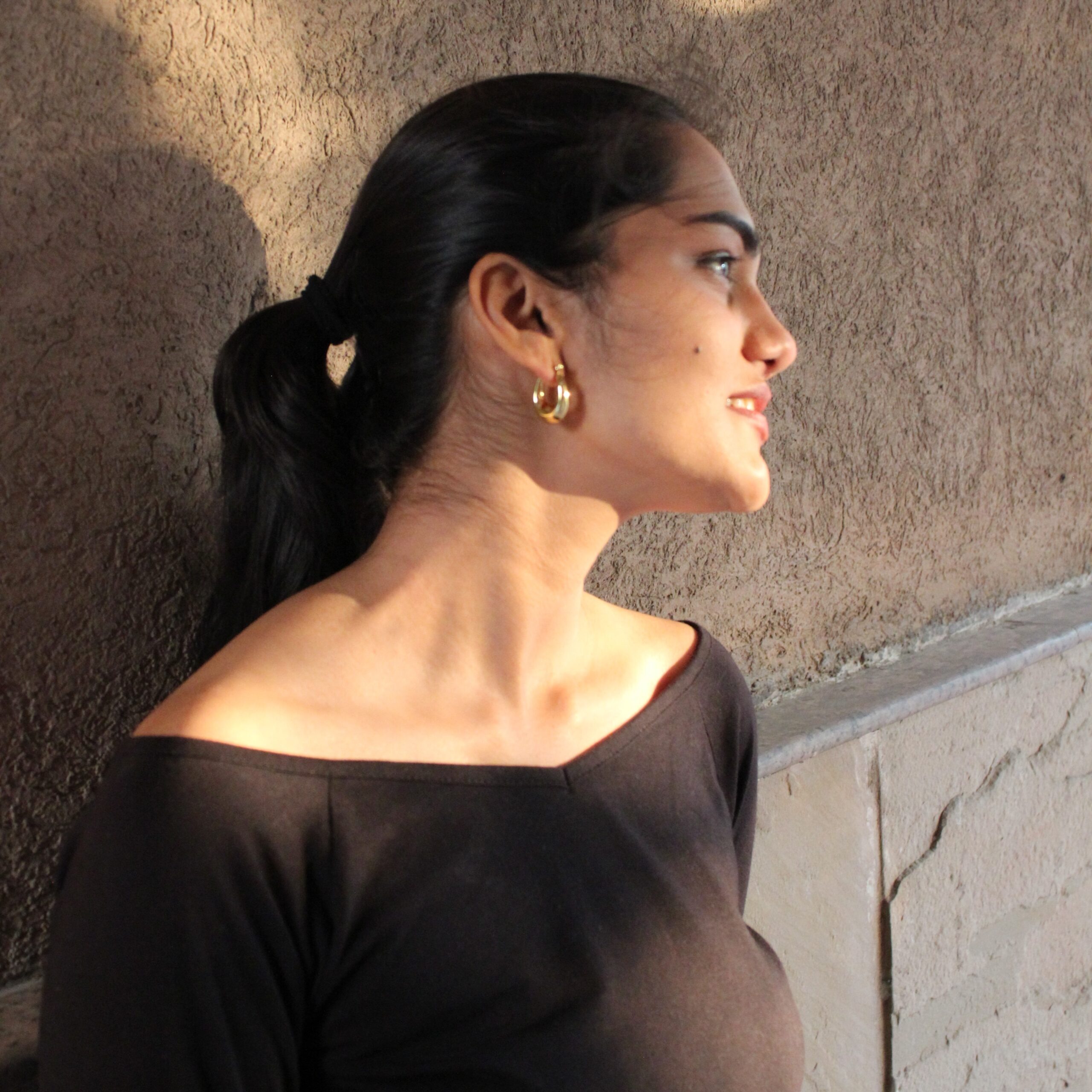 Close side view of Masaira Luna Drop gold-plated huggie hoops on ear, compact teardrop shape with hinged clasp.