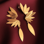 Phoenix gold-plated earrings with layered leaf design on maroon satin fabric