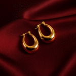 Masaira gold-plated puffed teardrop huggie hoop earrings on deep maroon satin fabric