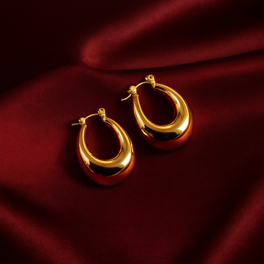 Masaira gold-plated puffed teardrop huggie hoop earrings on deep maroon satin fabric