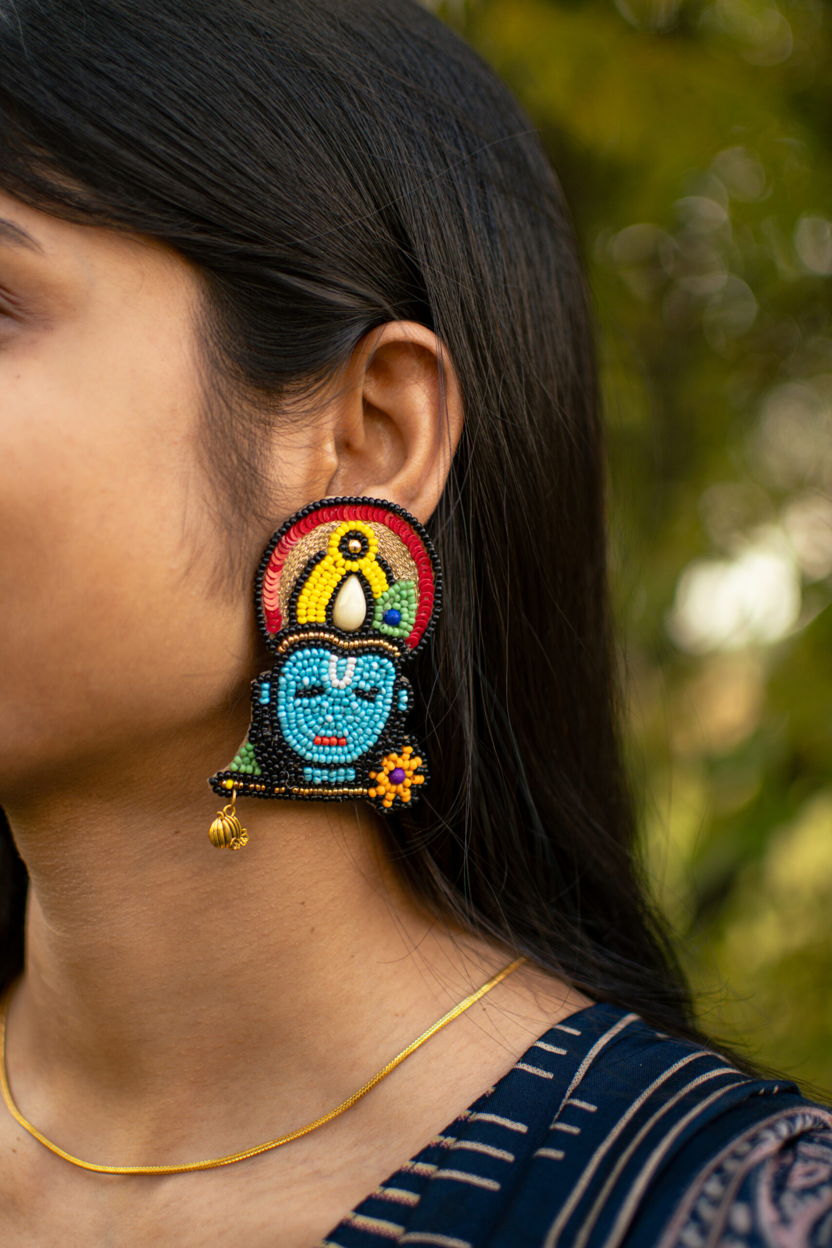 Close-up outdoor profile of model with straight hair wearing Krishna temple earrings in blue, red, yellow and gold beads — Masaira ethnic jewellery