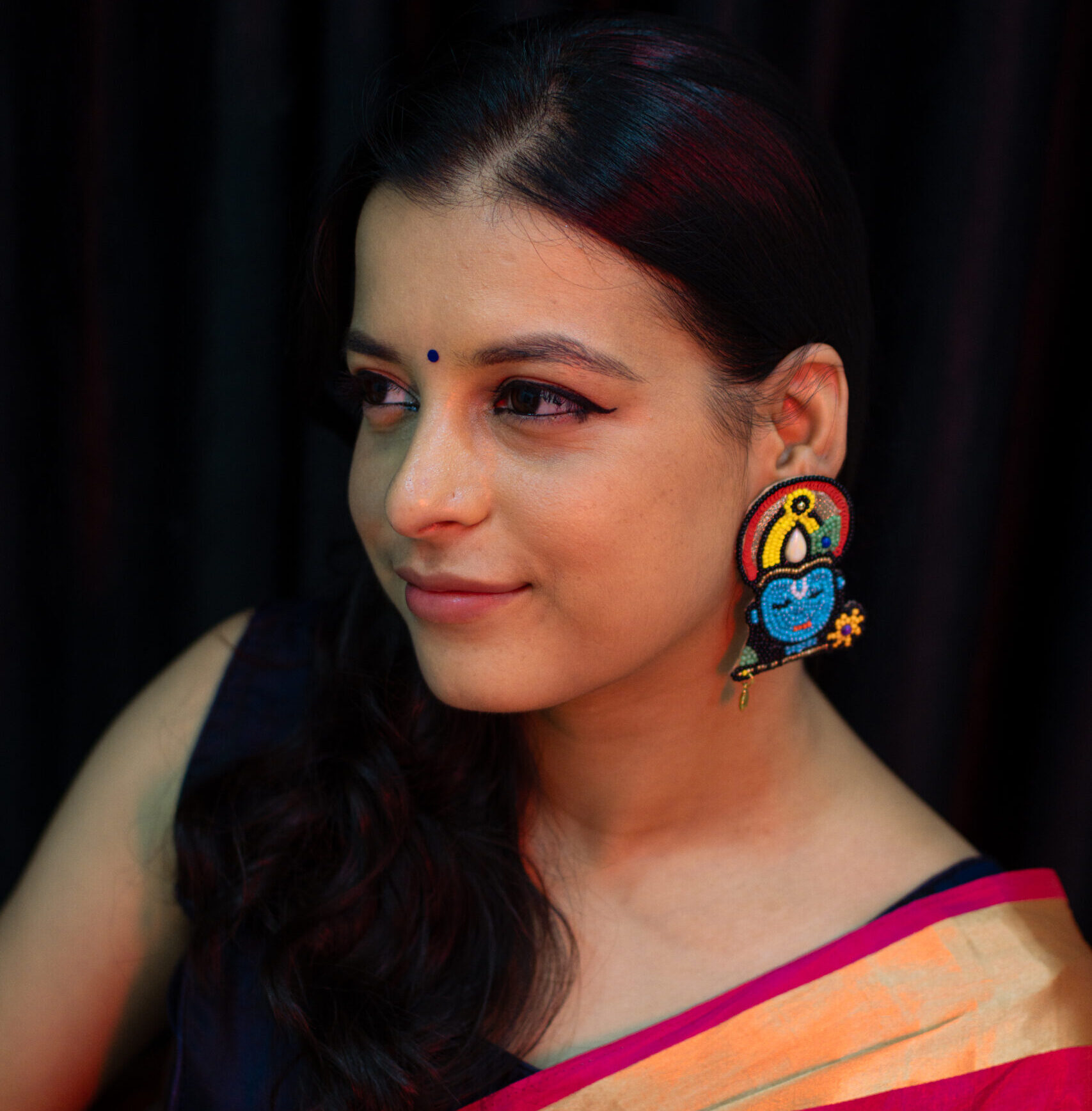Model in pink saree smiling softly while wearing Krishna motif beaded earrings — Masaira deity-inspired jewellery