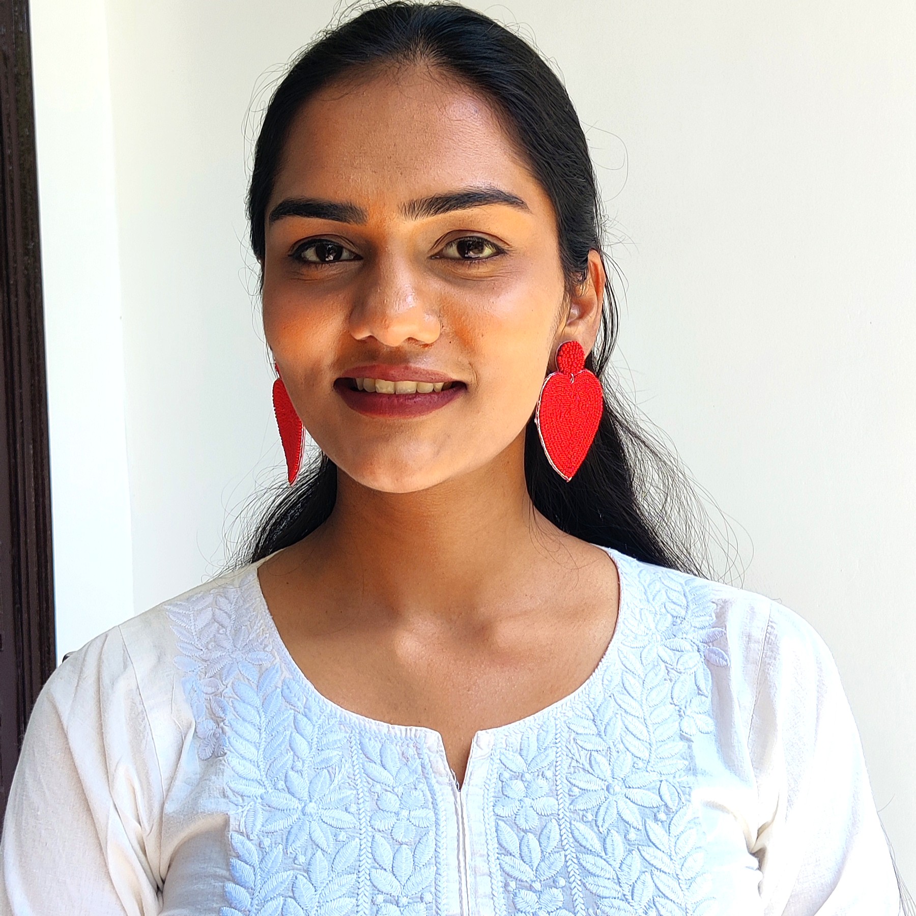 Smiling model in a white chikankari kurta wearing red beaded heart drop earrings — Masaira statement jewellery, front view