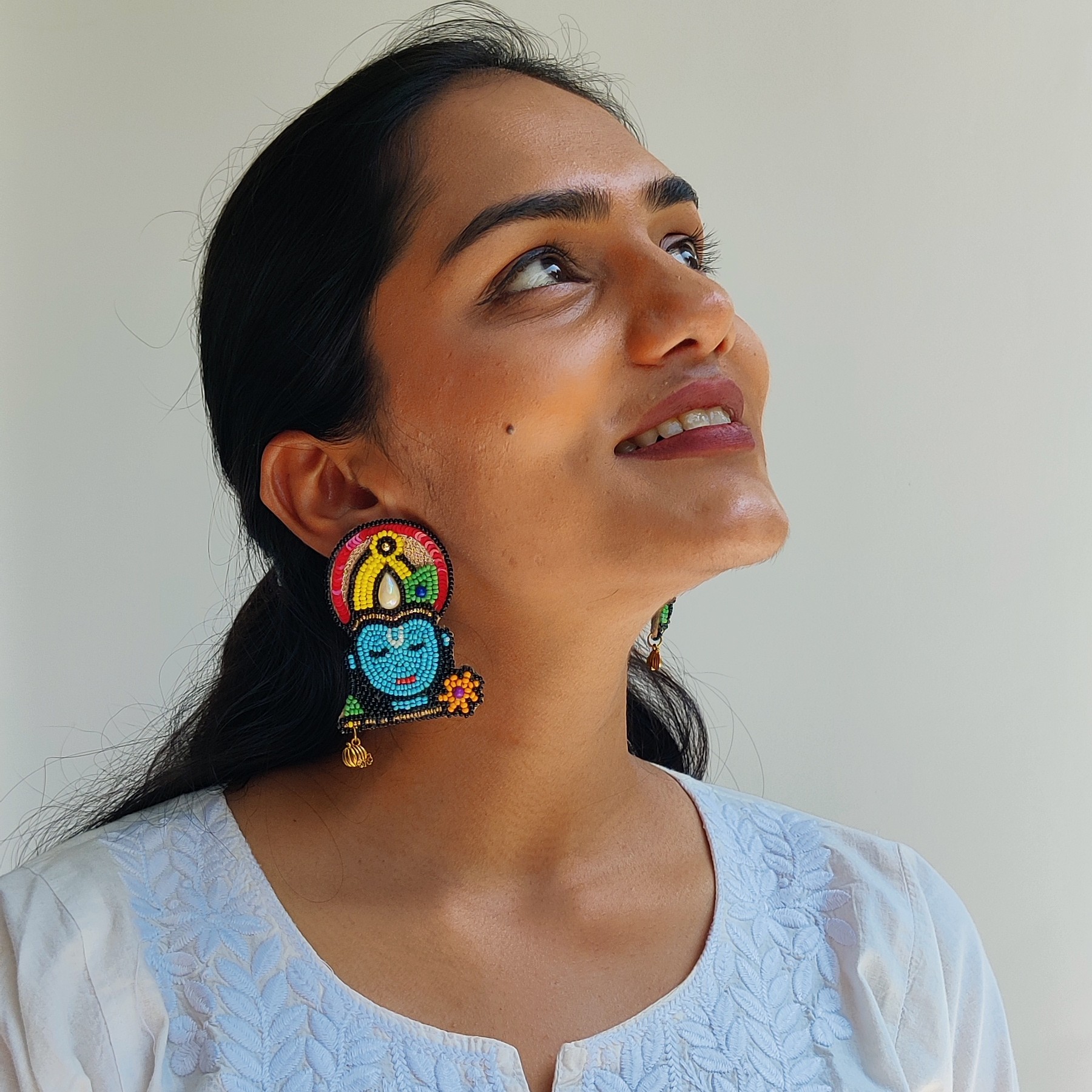 Model in white kurta looking upward with Krishna beaded earrings — vibrant deity-inspired ethnic jewellery by Masaira