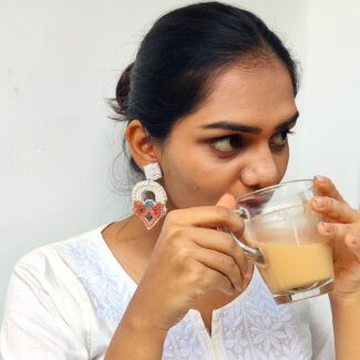 Woman wearing handcrafted beaded earrings while sipping tea – Shimmering Arch design