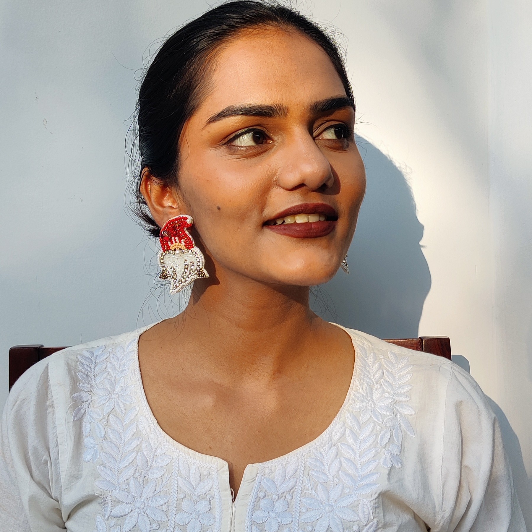 Woman in white wearing festive Santa hat earrings looking sideways