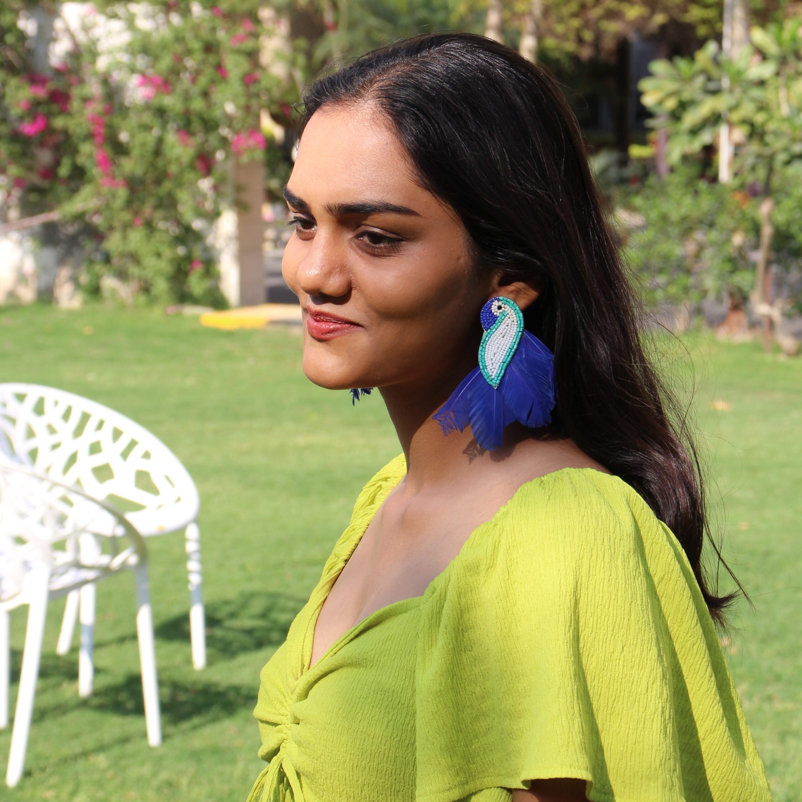 Statement Blue Feather Parrot Earrings – Worn Outdoors Indian woman wearing handcrafted blue feather parrot earrings in a sunlit garden.