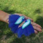 A pair of blue feather beaded parrot earrings resting in a woman's open palm.