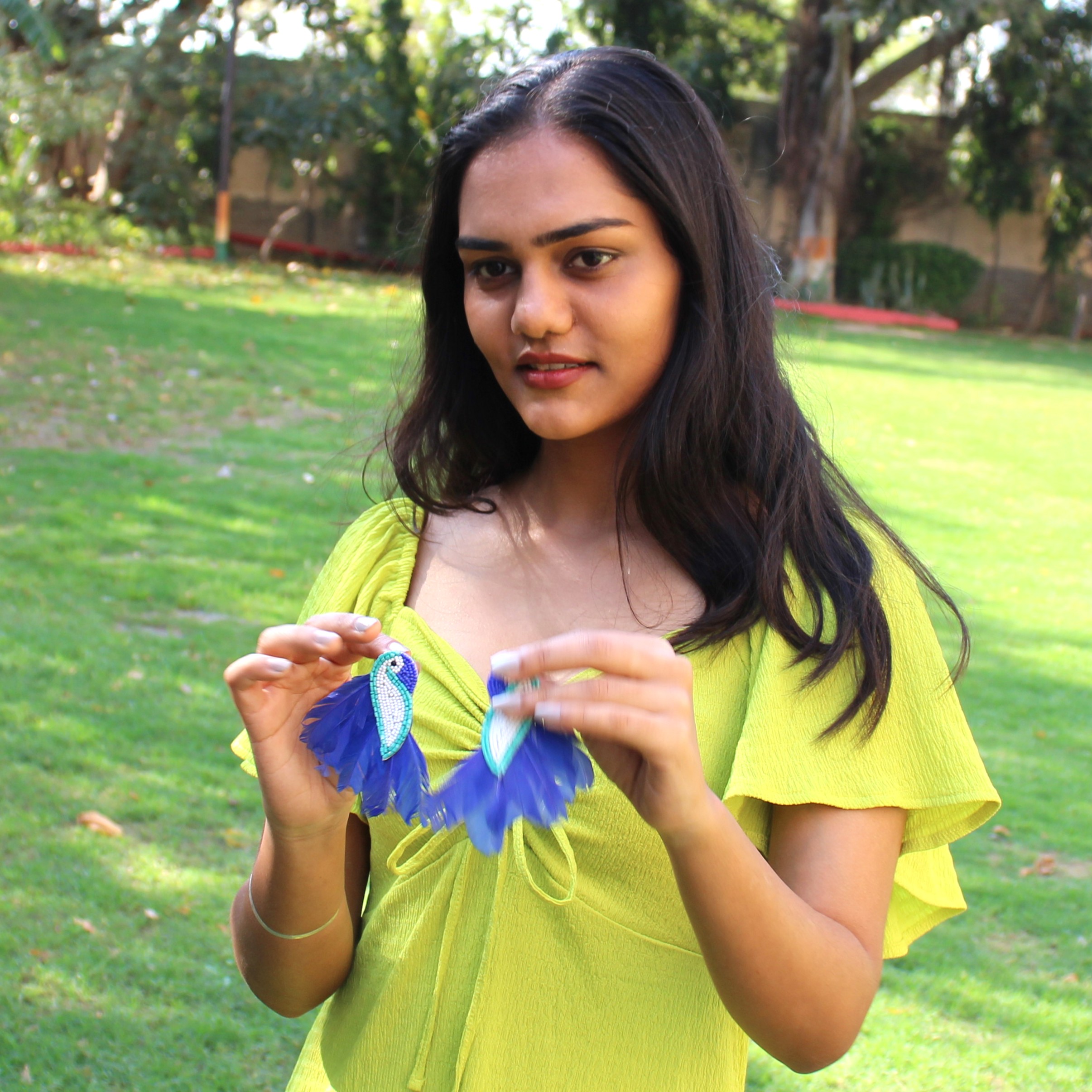 Handcrafted Parrot Earrings – Art in Your Palm Young woman holding a pair of beaded parrot earrings with blue feathers in her hands.