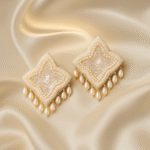 Handcrafted ivory beaded statement earrings with star-shaped sequins and pearl drop accents on a satin background.