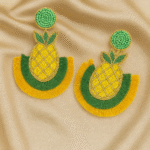 Flat lay of Masaira’s pineapple-shaped beaded earrings in yellow, green, and gold on satin background