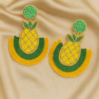 Flat lay of Masaira’s pineapple-shaped beaded earrings in yellow, green, and gold on satin background