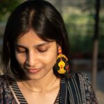 Close-up of an Indian woman smiling softly while wearing large handcrafted Kali earrings made with colorful seed beads.