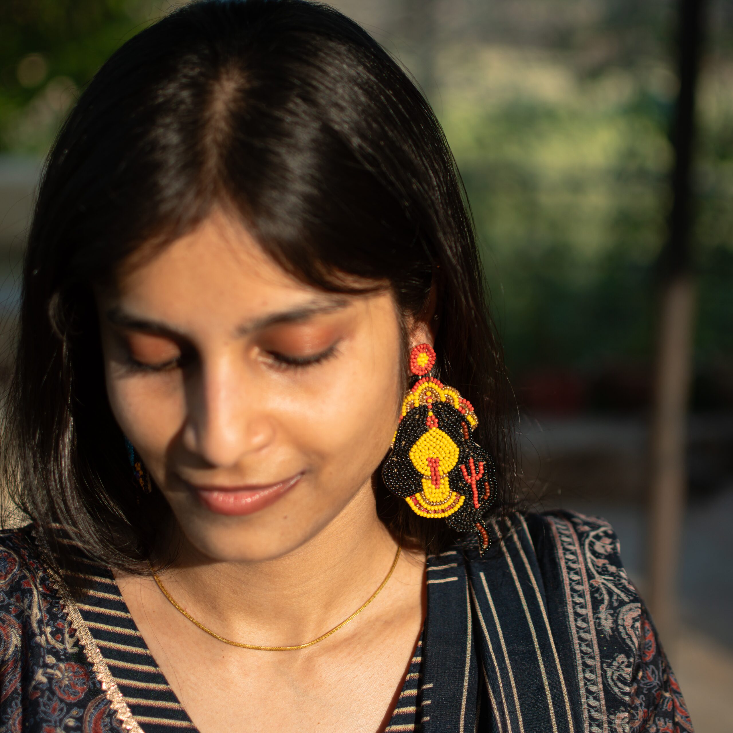 Close-up of an Indian woman smiling softly while wearing large handcrafted Kali earrings made with colorful seed beads.