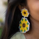Close-up of two-tiered sunflower earrings with seed bead embroidery on a woman with dark hair.