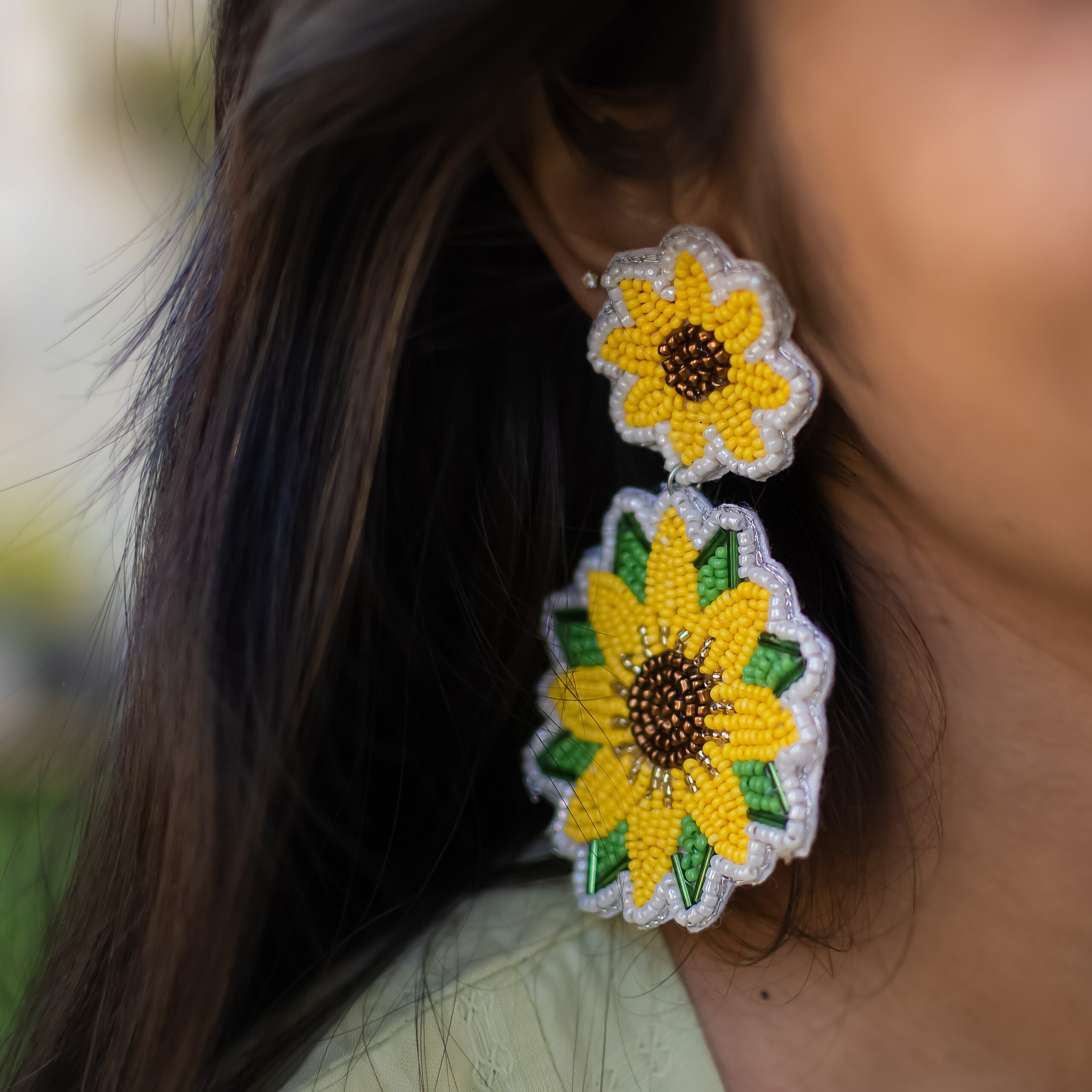 Close-up of two-tiered sunflower earrings with seed bead embroidery on a woman with dark hair.