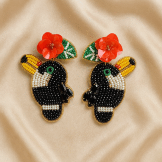 Beaded toucan earrings with red flower and yellow beak on satin fabric background.
