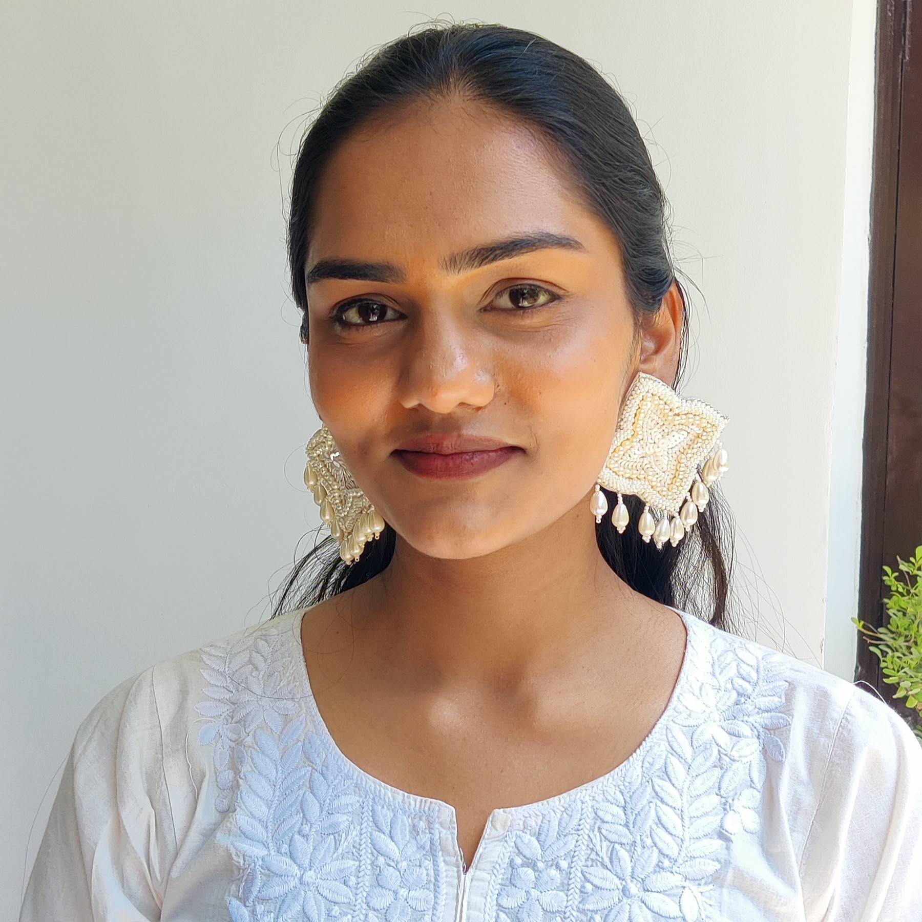 Close-up of a woman wearing handcrafted beaded square pearl earrings with dangling teardrop beads, smiling gracefully in natural daylight.