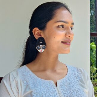 Handcrafted beaded earrings shaped like a woman's face with sunglasses and a bun hairstyle, placed on champagne satin fabric.