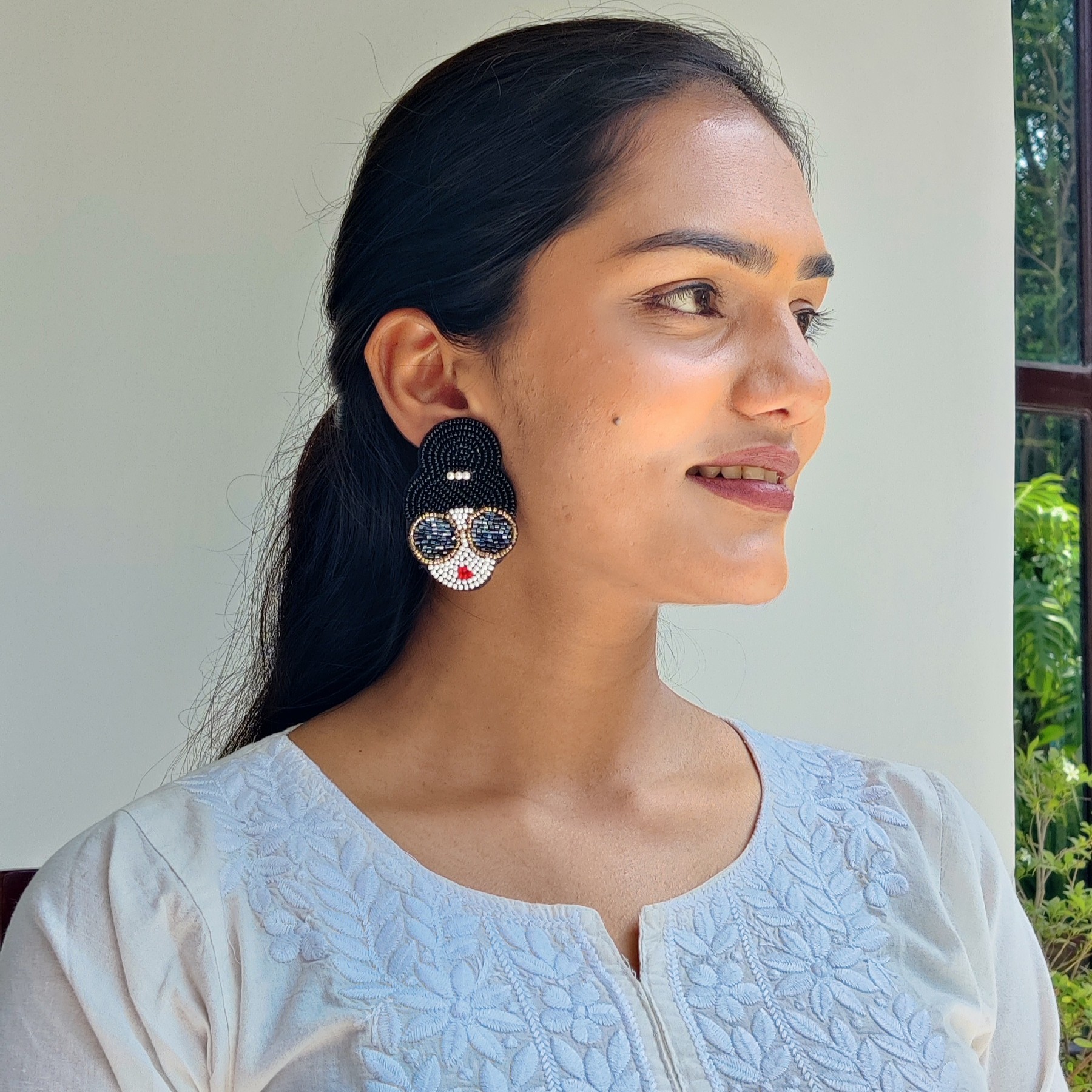 Statement Beaded Earrings – Sunglass Diva Design Handcrafted beaded earrings shaped like a woman's face with sunglasses and a bun hairstyle, placed on champagne satin fabric.