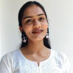 A pair of handcrafted beaded earrings shaped like a stylish woman’s face with black hair, pearl details, red lips, and oversized sunglasses, placed on champagne satin fabric.