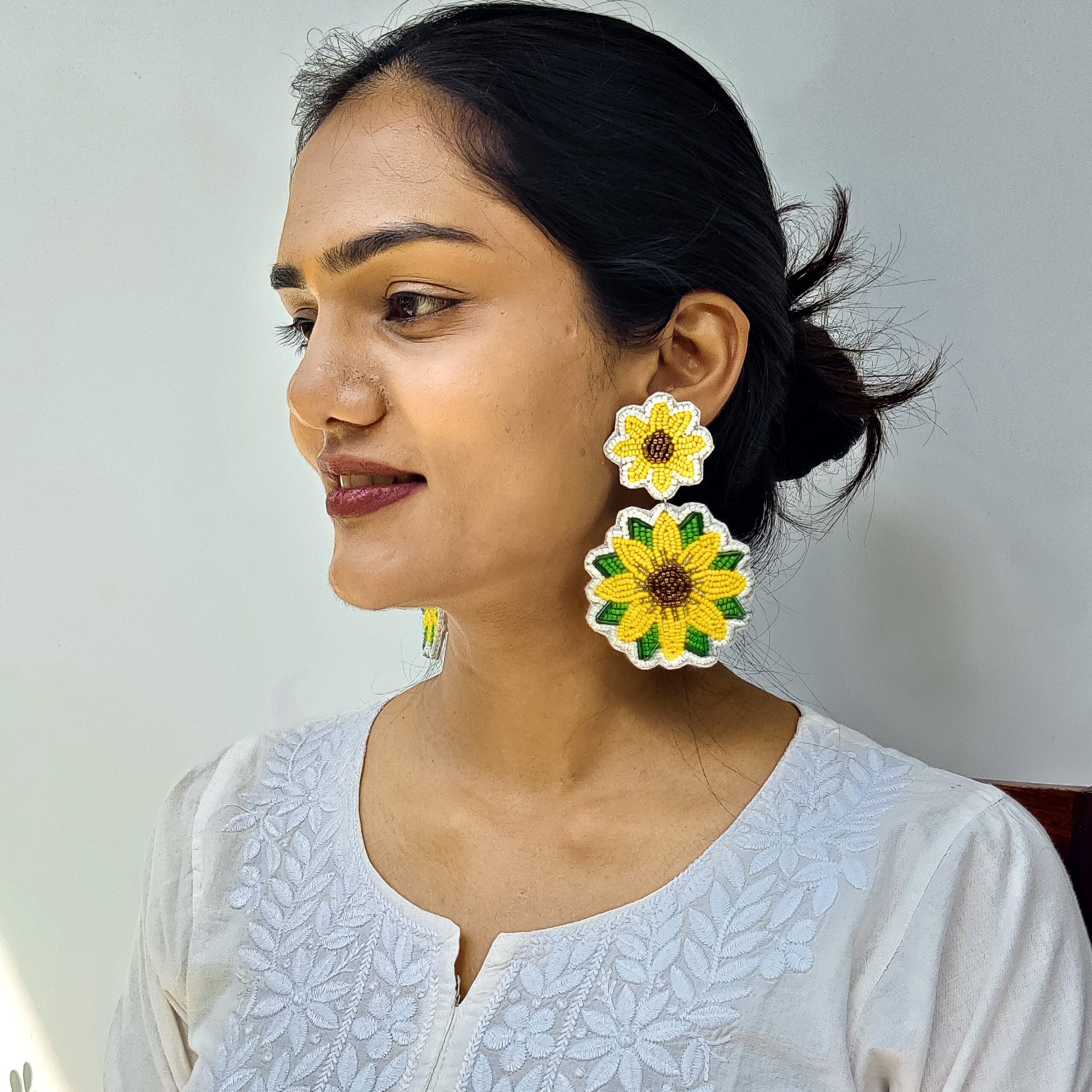 Indian woman with hair in a bun wearing oversized sunflower earrings, smiling in a white embroidered kurta.